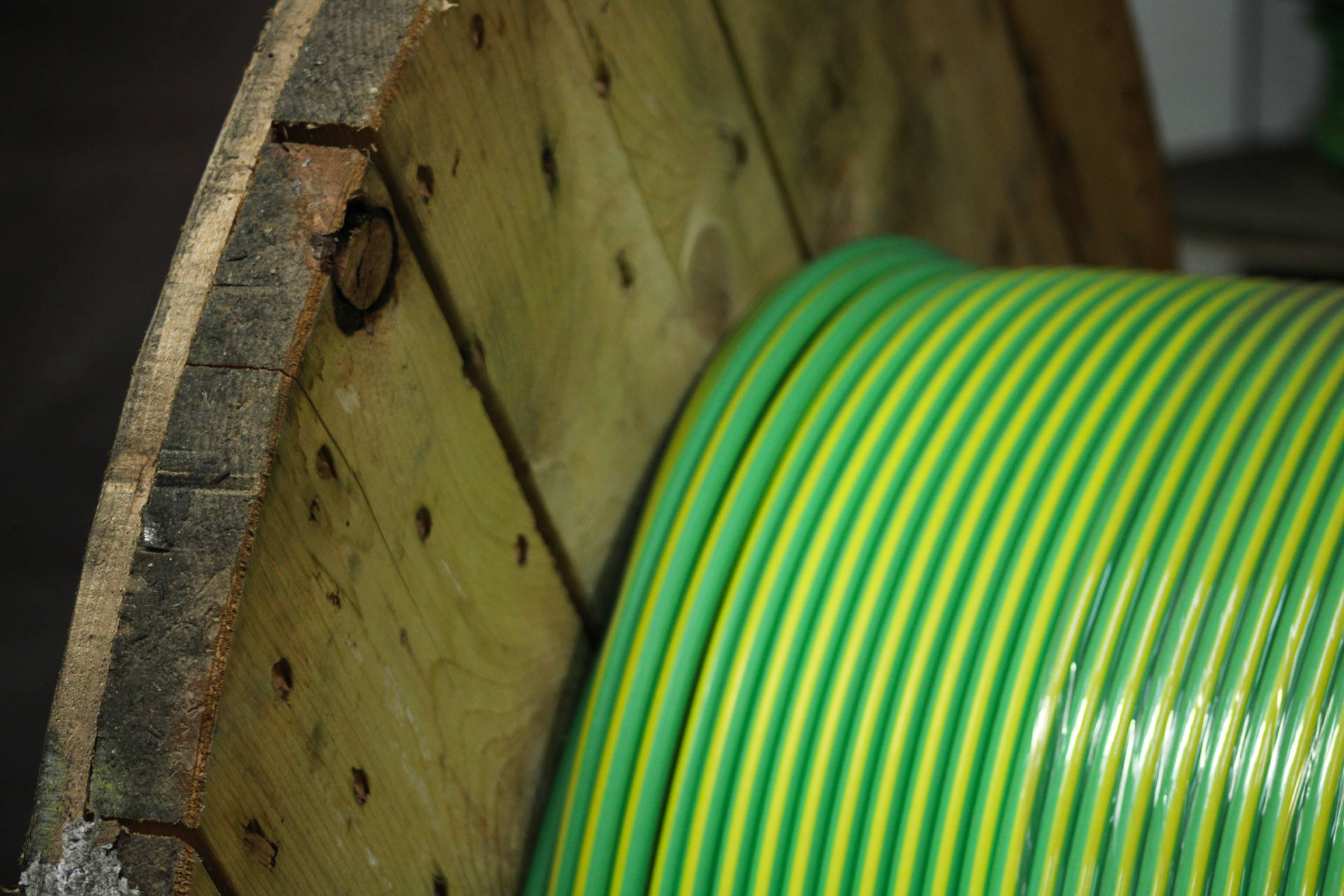 A close up section of green/yellow striped cable on a large wooden reel